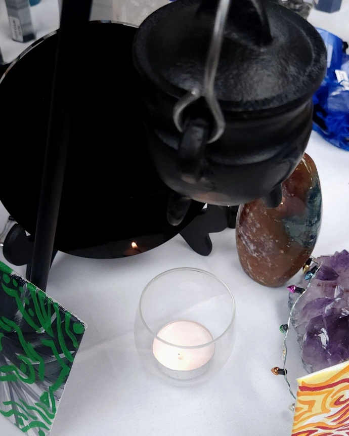 A candle glows beneath a cauldron and reflects in an obsidian scrying mirror
